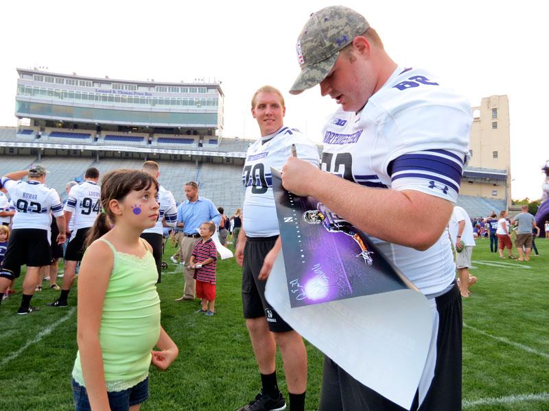 Offensive linemen Pat Ward (left) and Taylor Paxton (right) sign a young fans poster. (Ariel Yong/The Daily Northwestern)