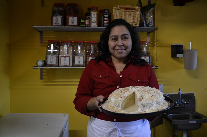 Tania Merlos-Ruiz, owner of Tomate Fresh Kitchen, poses with one of her cakes. Tomate is set to reopen Feb. 15.