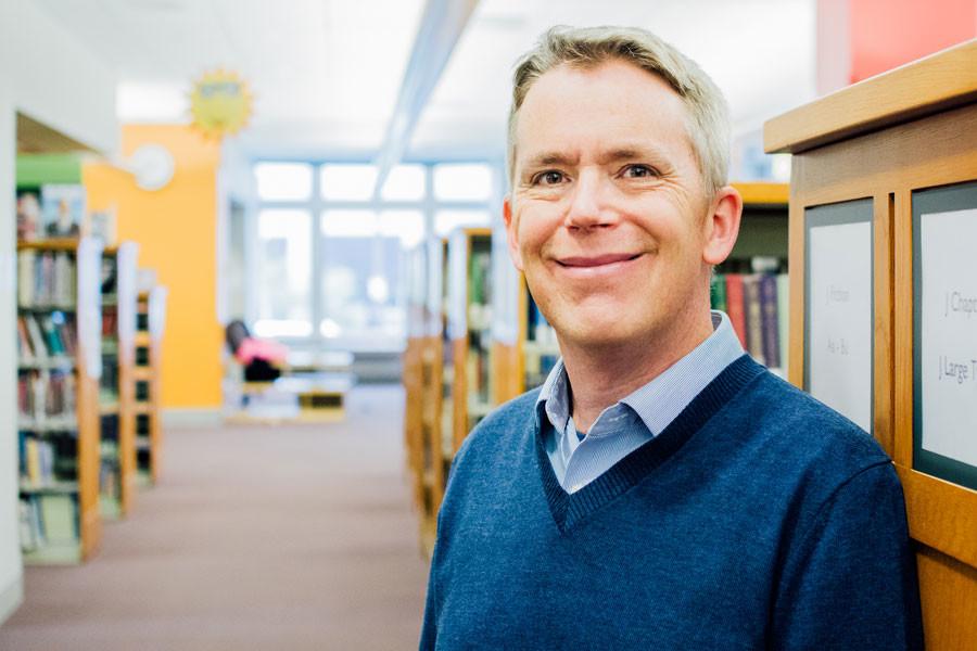 Brian Wilson, a children’s librarian, stands among stacks of books at Evanston Public Library. Wilson will start work for the 2017 Caldecott Award Selection Committee in January.