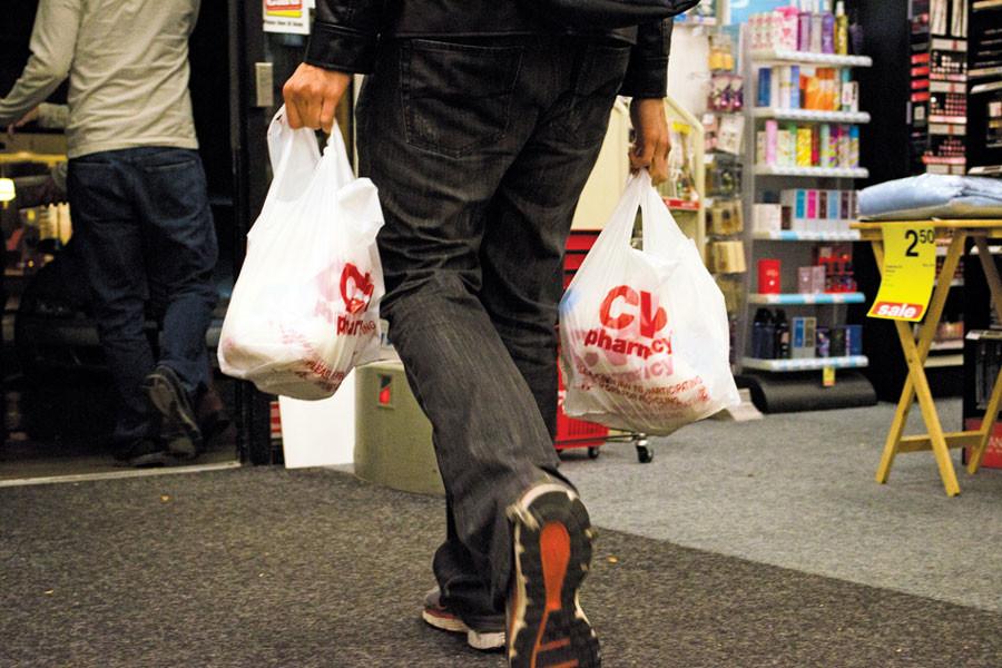 A man carries two plastic CVS bags out of the store.