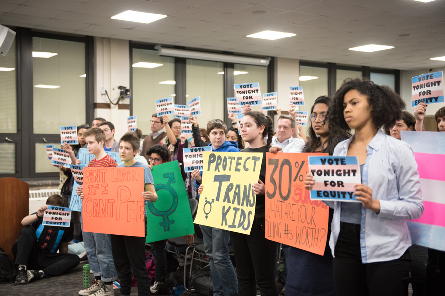 Students hold signs in support of a new transgender policy at a Monday meeting. The policy, which goes into effect in the fall, will allow transgender students to use the locker room of their choice.