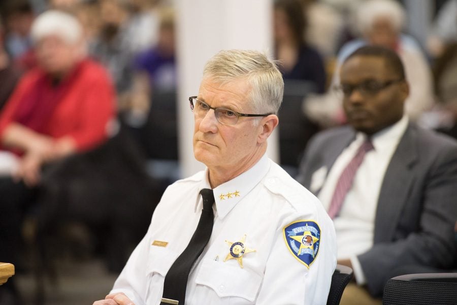 Richard Eddington sits in a chair during a city meeting. He is wearing a white police uniform.