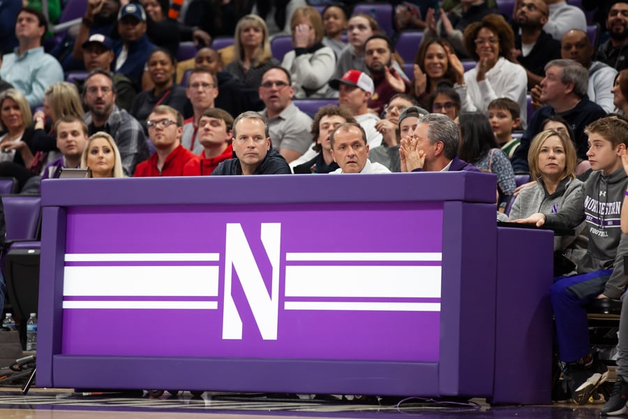 Chris Collins, Jim Phillips and Brian James sit at a basketball game. Northwestern has decided to play its weekend game despite the coronavirus. 
