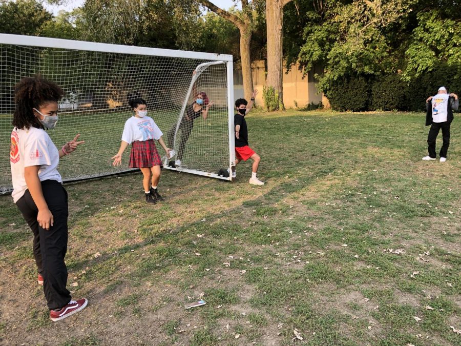 Five teens pose around a soccer goal, looking away from the camera.
