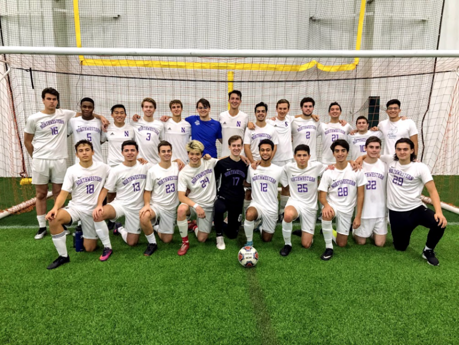 23 men dressed in white soccer uniforms that say Northwestern and their number in purple in front of a soccer goal. They are smiling with their arms around each other.