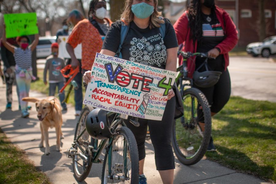 Allie Harned stands with a bike and a sign that reads “Vote 4 Transparency, Accountability, Racial Equity” and lists municipal election candidate names.