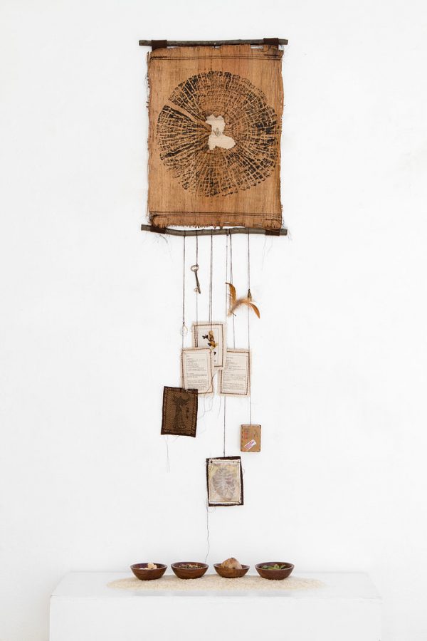 A+brown+scroll+of+papyrus+with+branches+on+the+top+and+bottom.+The+ink+on+the+papyrus+creates+a+circle+design.+Below%2C+there+are+various+hanging+objects.