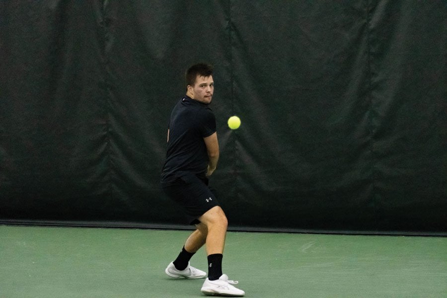 Northwestern men’s tennis player wearing a black shirt and black shorts returns a shot with his backhand