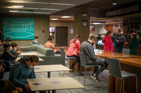 Students sitting at tables, on couches in a dimly lit facility, next to the Starbucks located within Norris University Center.
