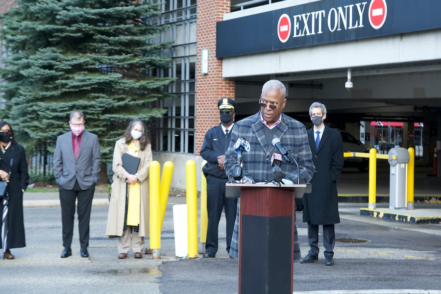 Rev. Michael Nabors speaks at a podium outside a parking garage. Four speakers, all wearing masks, stand in a line behind him.