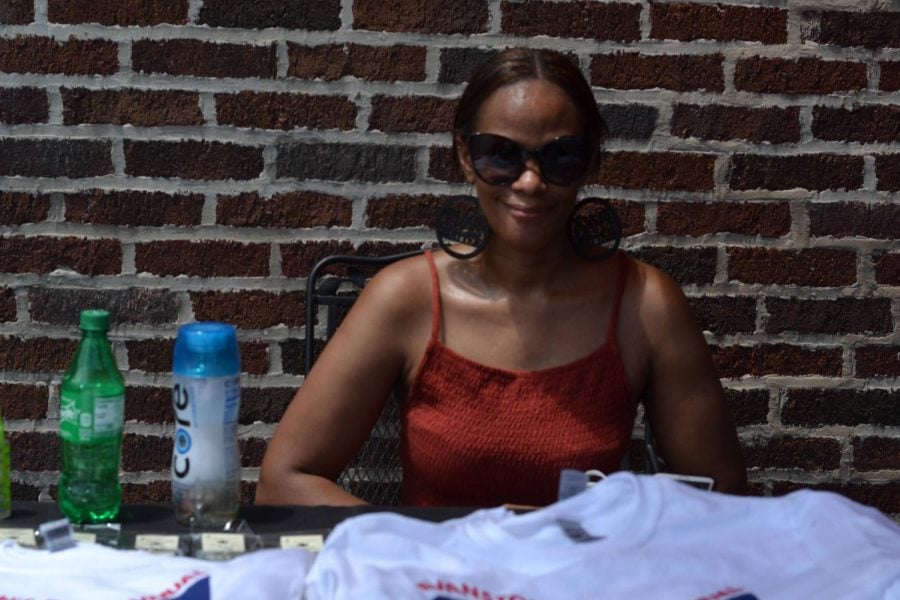 Kemone Hendricks sits outside in front of a brick wall at a table selling merchandise at a Juneteenth pop-up shop.