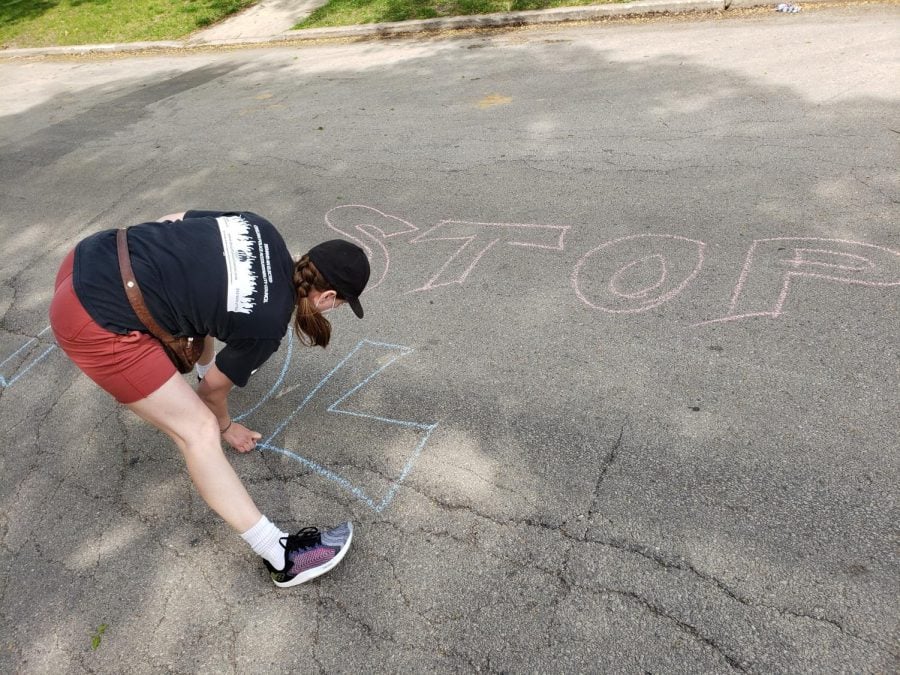A woman crouches while writing a protest message in chalk on Elmwood Avenue outside of the Evanston Police Department building.
