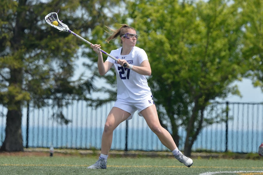 A lacrosse player wearing white with hair in ponytail gets in shooting position with the ball in her stick
