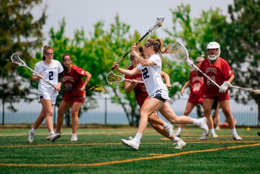 A+lacrosse+player+wearing+white+with+hair+in+ponytail+shoots+ball.