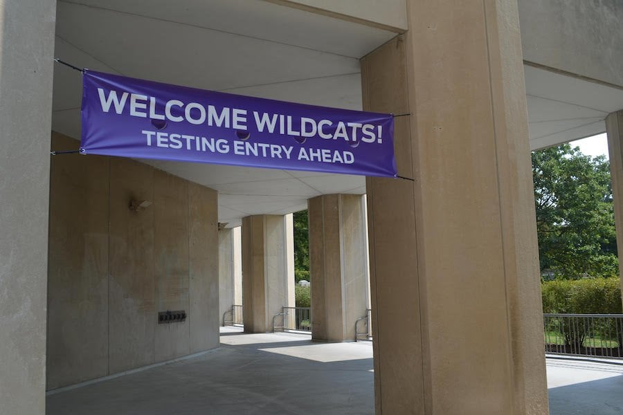 A+gray+and+tan+walkway+with+five+visible+pillars.+A+purple+banner+reads%3A+%E2%80%9CWelcome+Wildcats%21+Testing+Entry+Ahead.%E2%80%9D