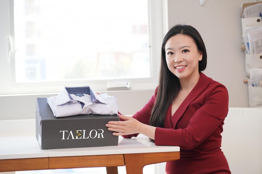Anya Cheng sits on the right side, wearing a burgundy suit. She holds a gray rectangular box with the words “Taelor.”
