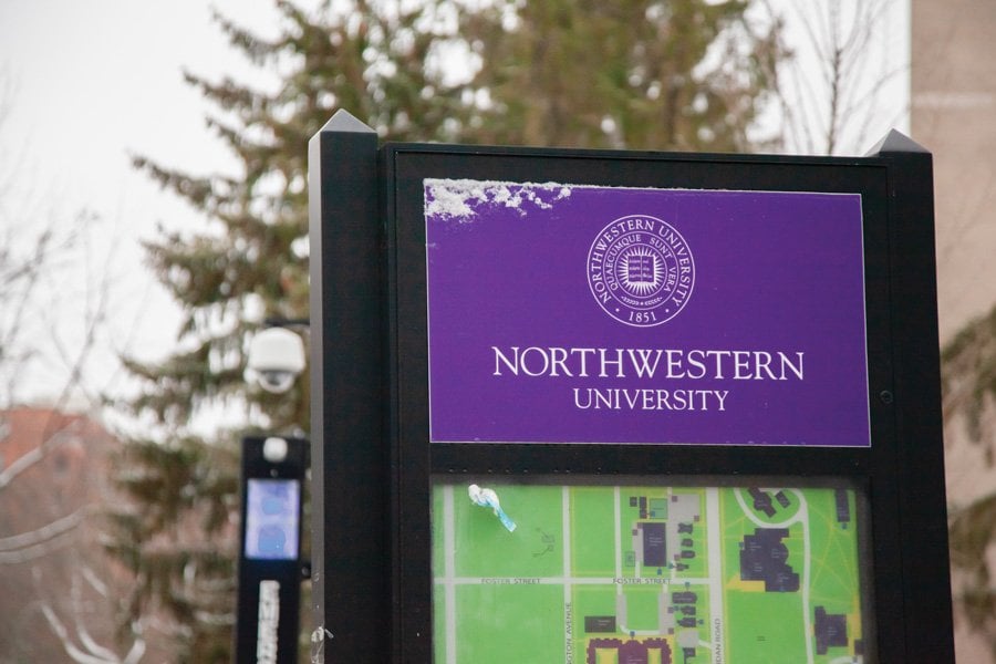 A black metal marker displays a purple sign with words “Northwestern University.” Below the sign is a green map of the campus. Behind the marker are dark green leaves and a lamppost.