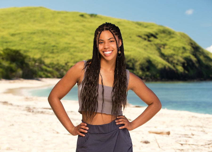 Liana Wallace stands in front of a beach and hill with her hands on her hips.