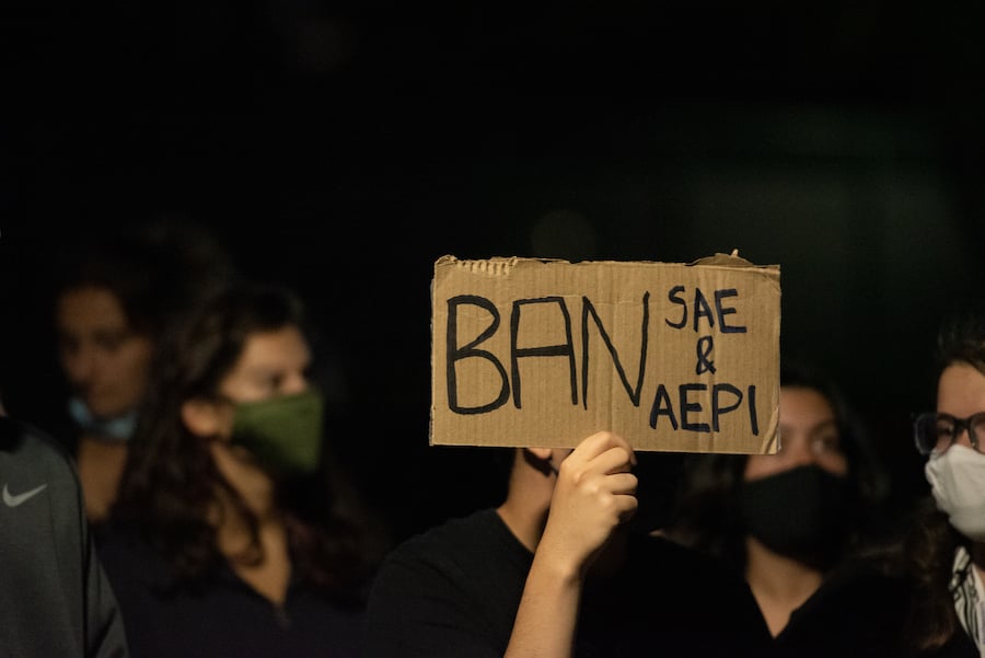 A student holds a cardboard sign that reads “Ban SAE and AEPi.”