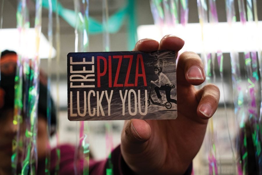 A hand holding up a coupon for a free Blaze Pizza in front of shiny streamers.