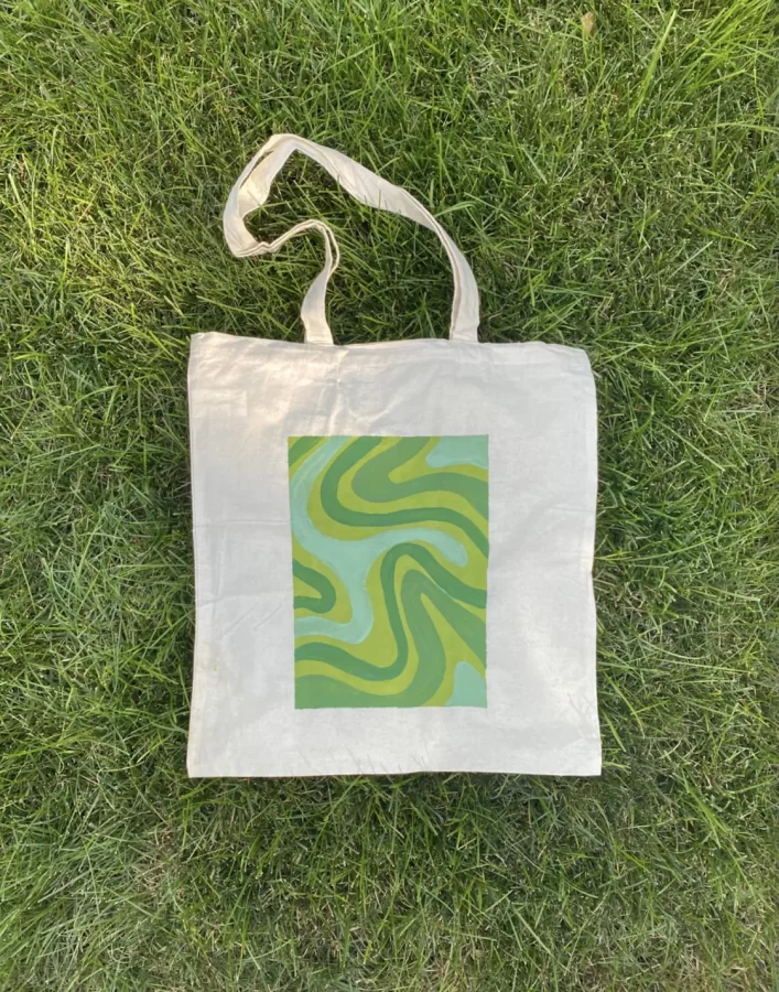 A canvas tote bag with a green-and-blue swirl pattern placed against green grass.