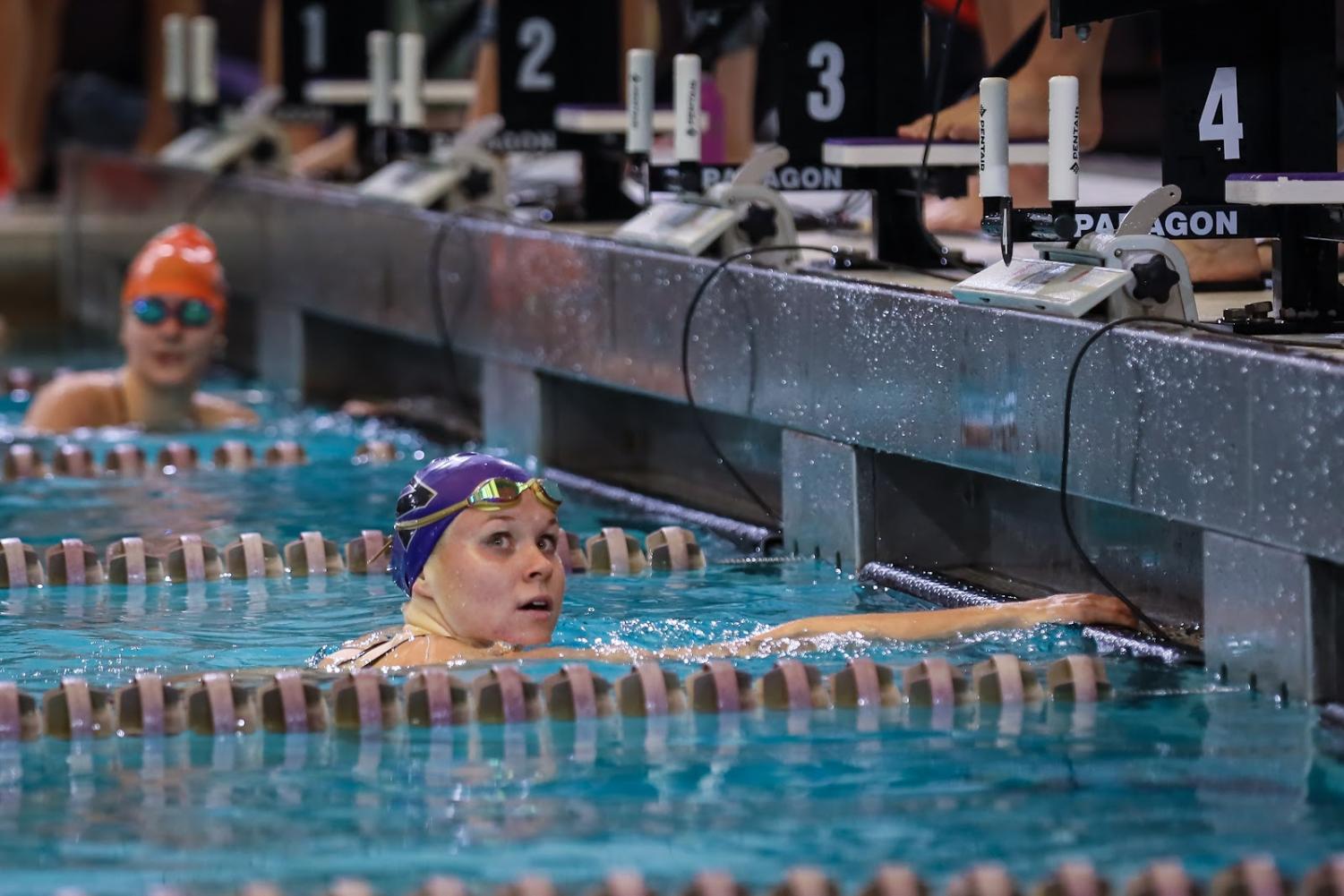 A Northwestern swimmer at the edge of the pool hangs their arms on the starting block while looking to the side. 