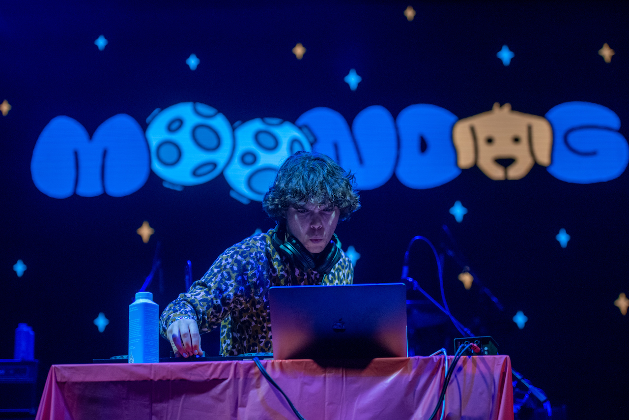The DJ stares at his laptop on stage, with the word “MOONDOG” up on the screen behind him.