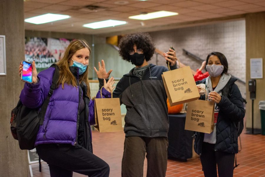 Three students hold brown bags with the text “scary brown bag” on them and face toward the camera.