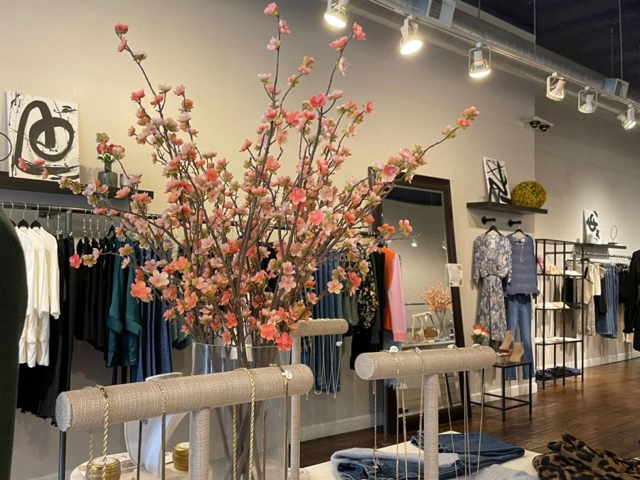 A+bright+pink+flower+sits+by+racks+of+jewelry+with+necklaces+in+the+middle+of+Madison+Grace.+Women%E2%80%99s+clothing+and+a+mirror+sit+in+the+background.