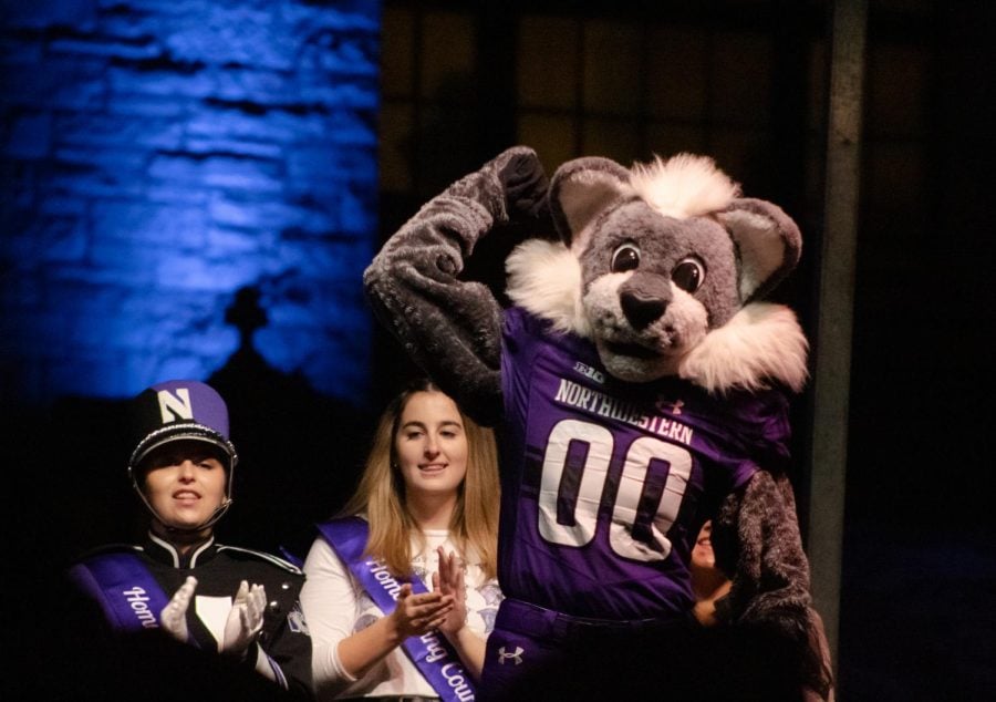 Two people in Northwestern Merch stand in front of an inflatable Willie the Wildcat taking a selfie with a phone in a red case.