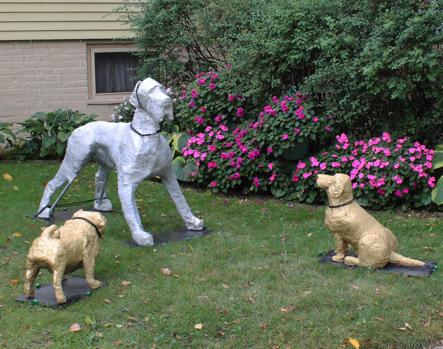 Three+sculptures+on+grass.+A+silver+great+dane+stands+over+a+gold+foil+pug+and+beagle.