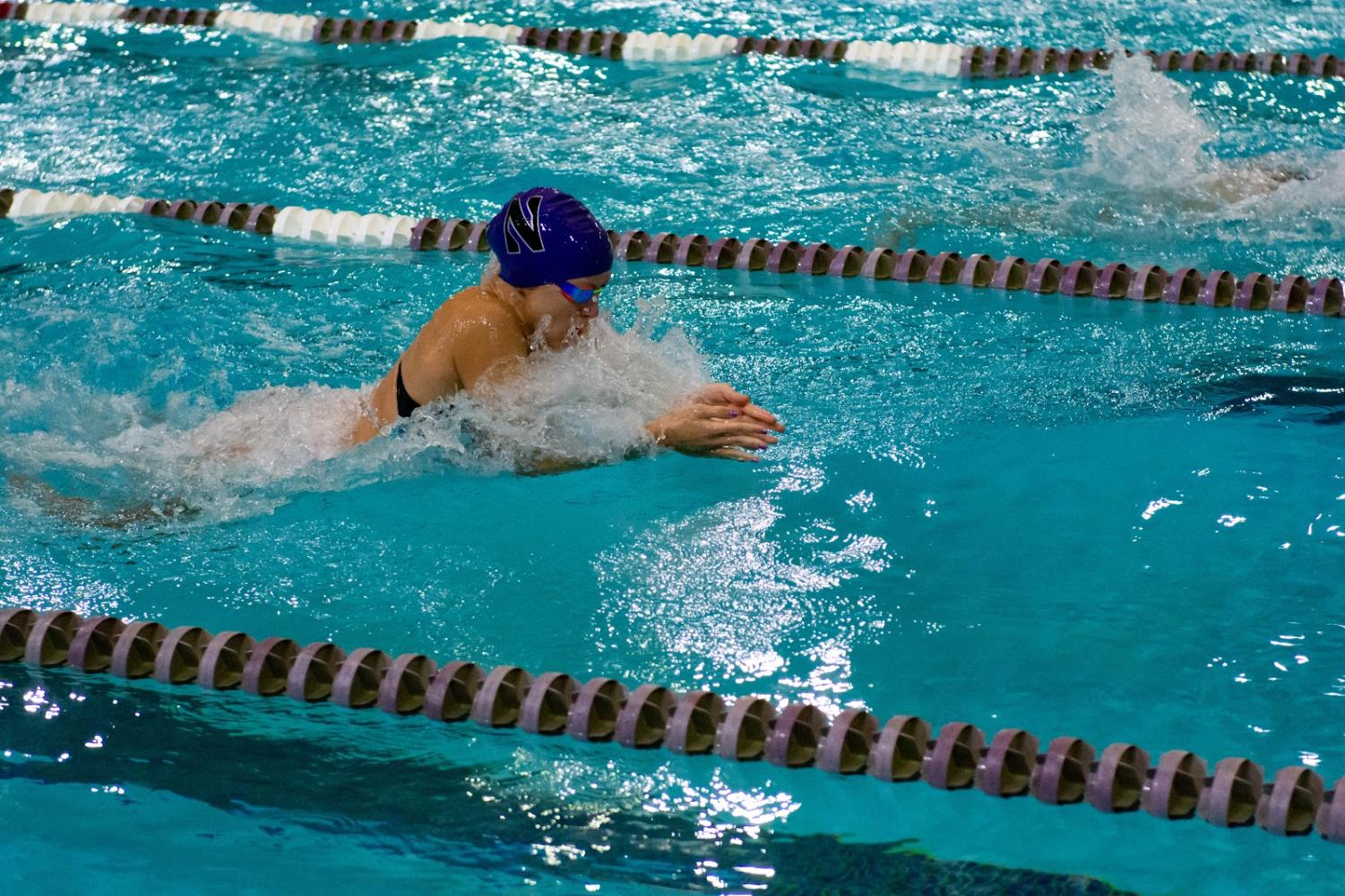 A swimmer wearing a purple swim cap takes a breath above the water during the race. 