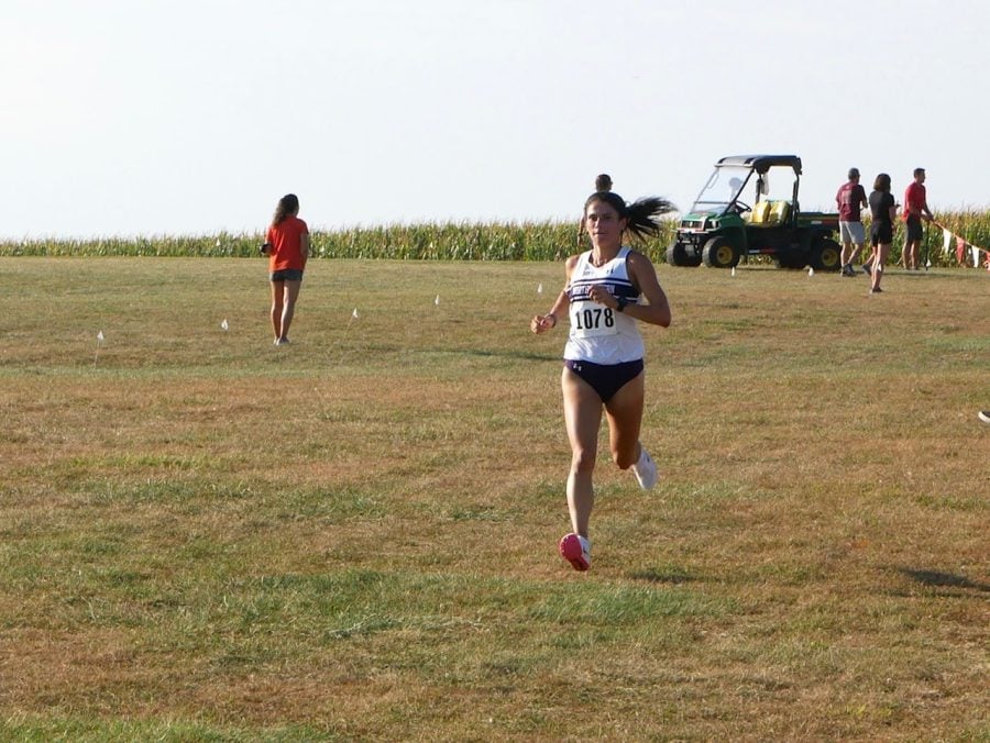 A girl with brown hair wearing a white singlet runs on a course with no one else around her.