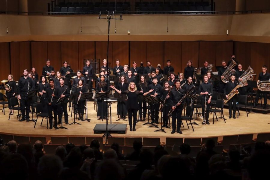 A blond professor takes a bow in front of a student orchestra dressed in all black.