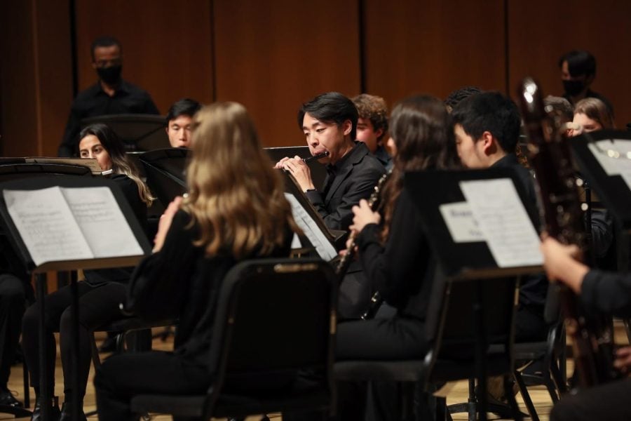 A student plays a piccolo in an orchestra dressed in all black.