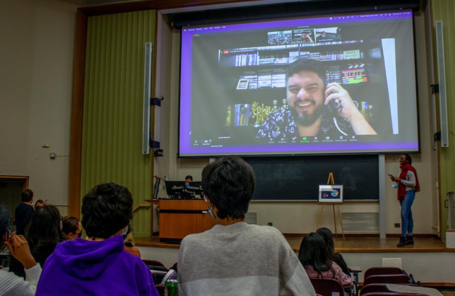 “Pacarette” director Allan Deberton, wearing a black patterned shirt, is projected on a large screen as he answers questions via Zoom. Various audience members can be seen viewing the presentation.