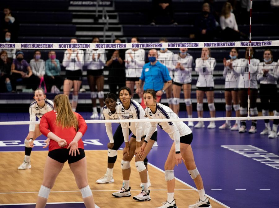 Charlotte Cronister, Temi Thomas-Ailara, Leilani Dodson and Alexa Rousseau stand with their knees bent behind a net on a volleyball court across from an Ohio State player.