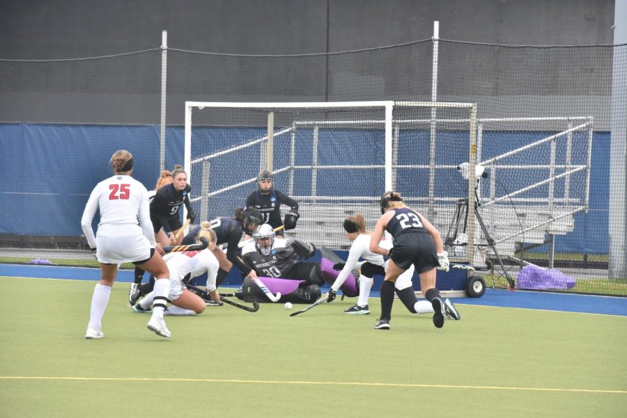 Players in black uniforms lunge to stop a shot in front of the goal.