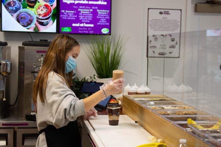 A woman with blonde hair wearing a grey sweatshirt squeezes a sauce out of a bottle into an açaí cup.