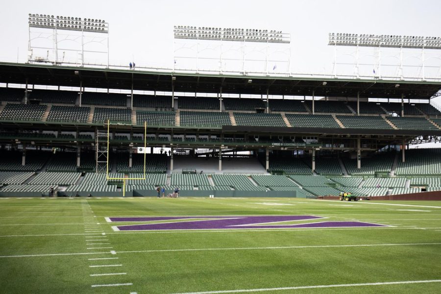 A football field with a purple “N” painted in the middle and a yellow goal post at the end, with two tiers of green seating in the background.