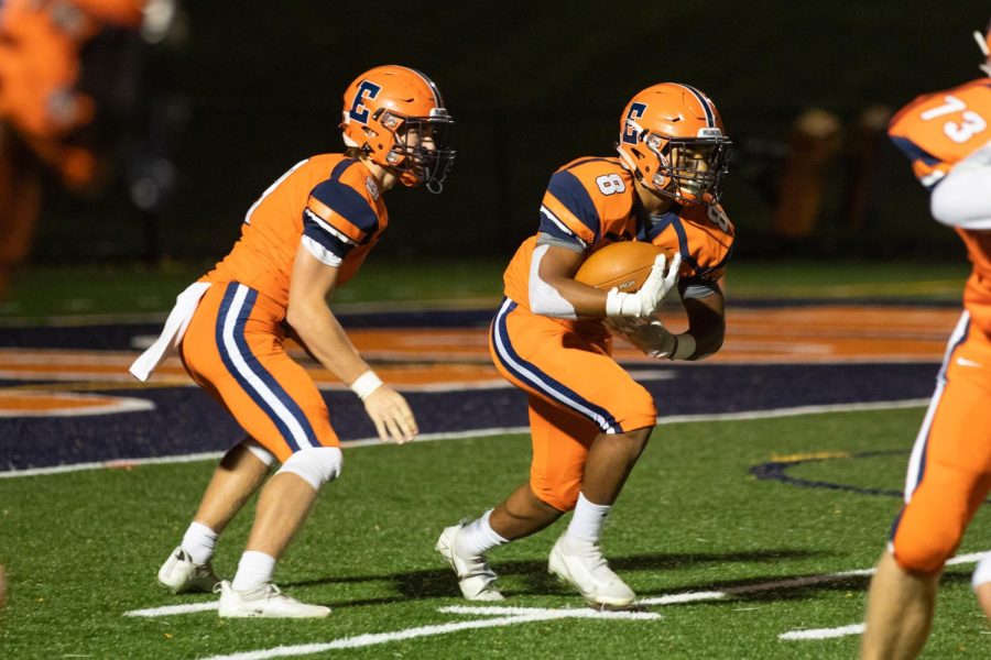Two football players wear orange-and-navy ETHS uniforms on a turf field.