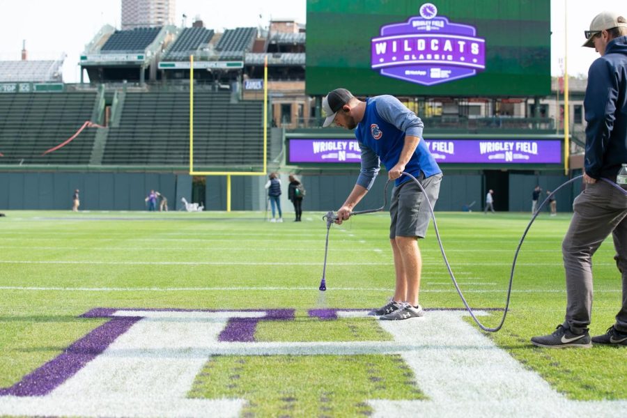 A person in a blue Chicago Cubs shirt sprays purple paint onto a football field.