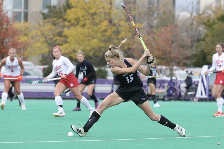 Girl with blonde hair in a ponytail in black uniform hits ball with stick.