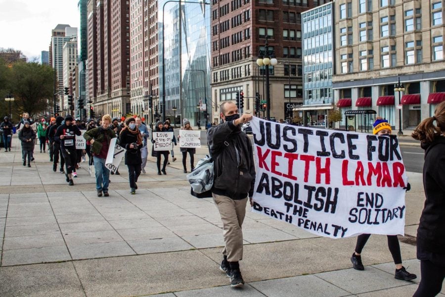 Ahead of a large group of people, two people walk and hold a large banner that reads “Justice for Keith LaMar,” “Abolish the death penalty” and “End solitary.”