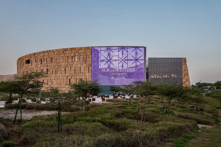 Picture of the NU-Q campus with greenery in the foreground and a large purple banner that reads “Northwestern University in Qatar.”