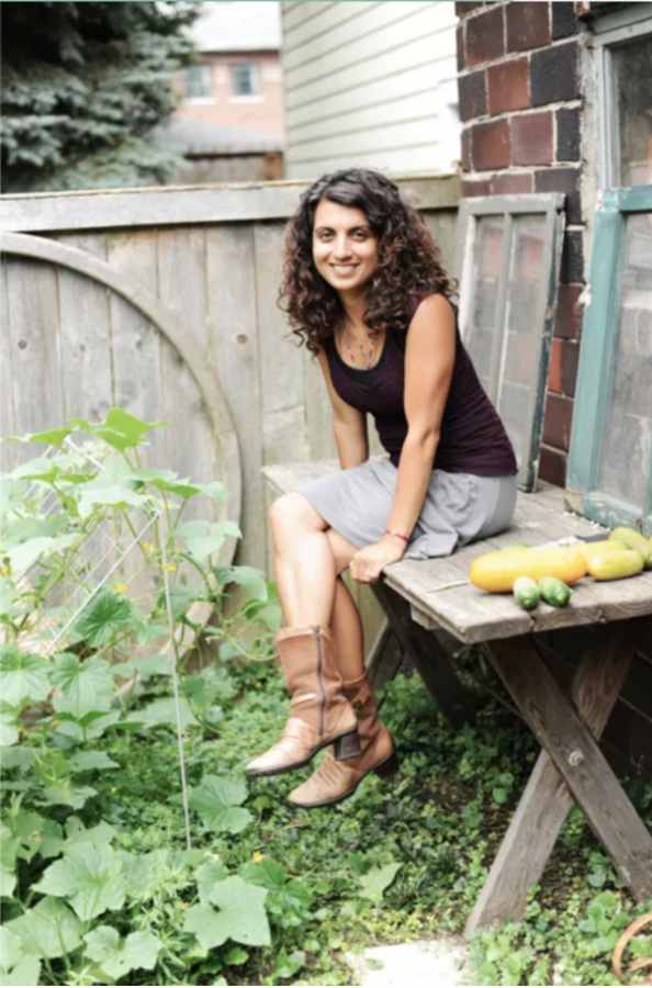 Dr. Geeta Maker Clark sits on a bench in a garden with squash and cucumbers to her right.