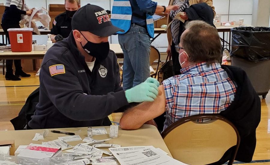 An Evanston Fire Department employee bandages a community member after administering a COVID-19 vaccine dose at a city vaccination event.