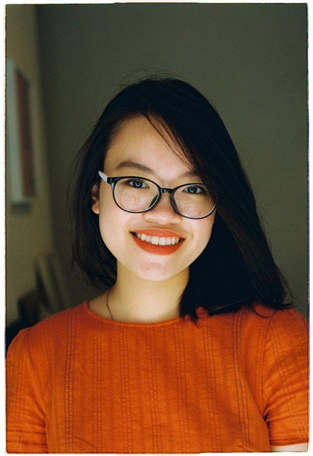 Sam Nguyen, a current fellow for the Public Interest Program, poses for a headshot in an orange top with a gray background.