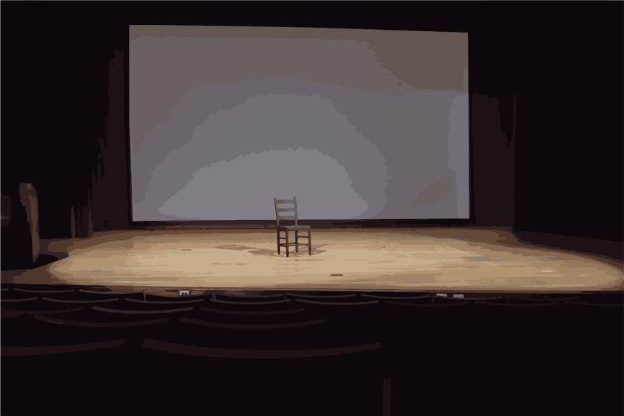 In a theatre, a black chair sits in the center of the stage with a spotlight on it.
