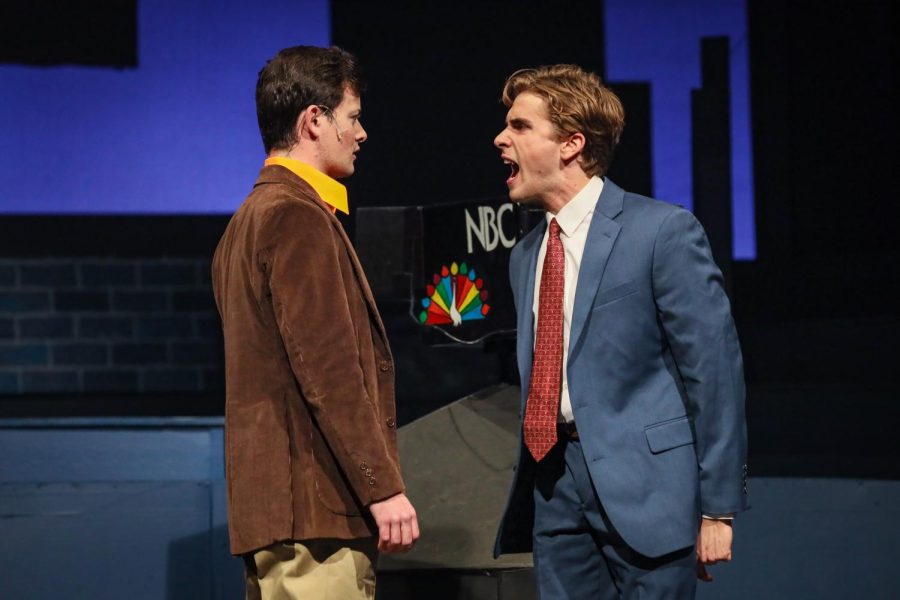 Two people argue. One wears a blue suit and red tie and yells at the other, who is dressed with a brown jacket and yellow shirt. An NBC logo can be seen behind them.